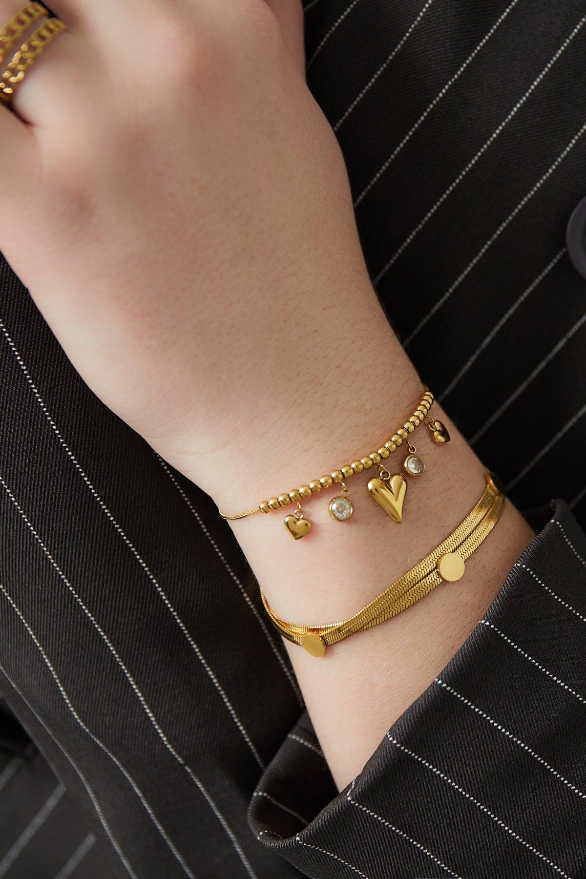 Close-up of wrist wearing gold heart bead bracelet paired with another gold bracelet on striped sleeve
