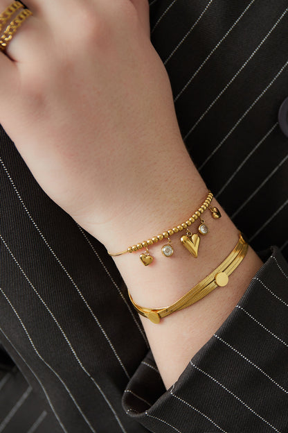Close-up of wrist wearing gold heart bead bracelet paired with another gold bracelet on striped sleeve
