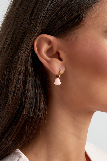 Close-up of woman's ear wearing gold hoop earring with soft pink enamel heart charm
