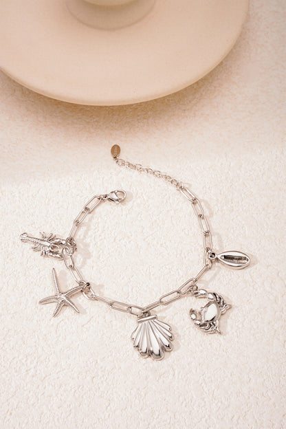Gold and silver toned seaside charm bracelets displayed side-by-side on textured cream surface