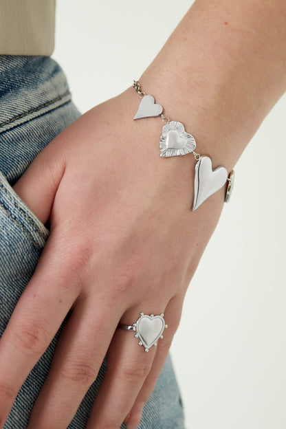 Close-up of a woman's wrist wearing the silver chunky heart charm bracelet paired with a silver heart ring, showing detailed charm textures