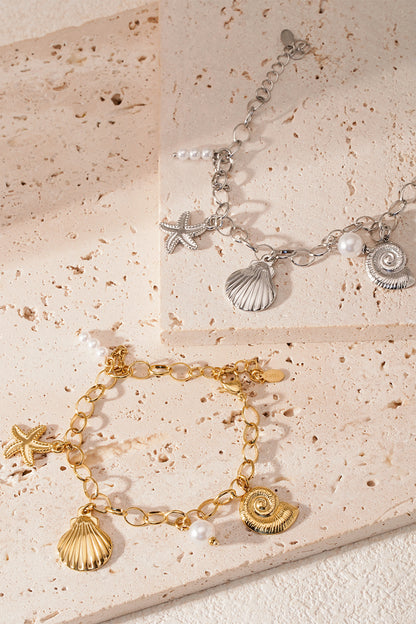 Close-up of gold and silver seaside charm bracelets styled on beige stone tiles with soft natural lighting
