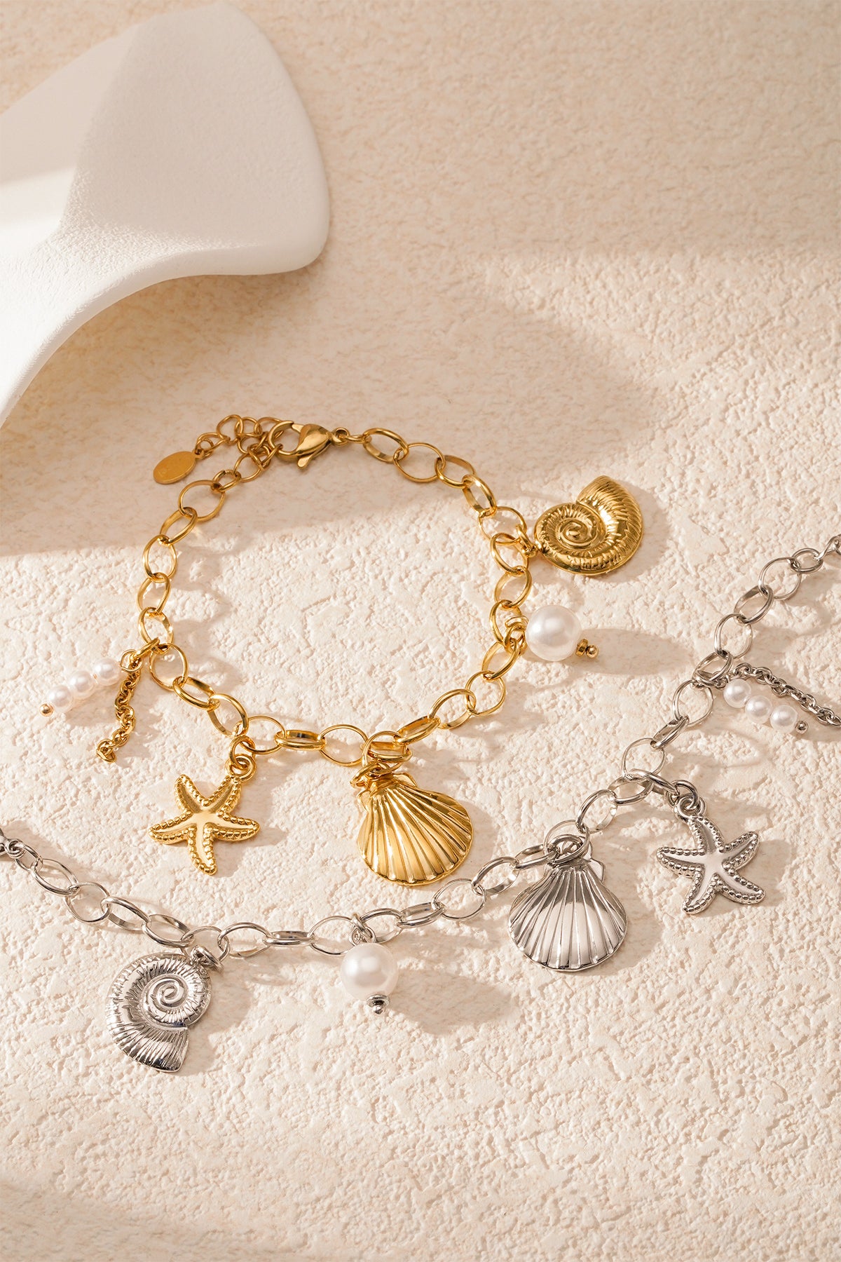 Detailed view of silver seaside charm bracelet with starfish, scallop shell, nautilus shell and pearl charms on white background