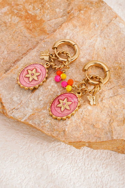 Pair of gold hoop earrings with pink flower pendants and colorful beads resting on textured tan stone surface