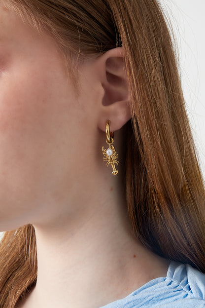 Woman wearing gold lobster charm earrings with pearl accent shown from side profile