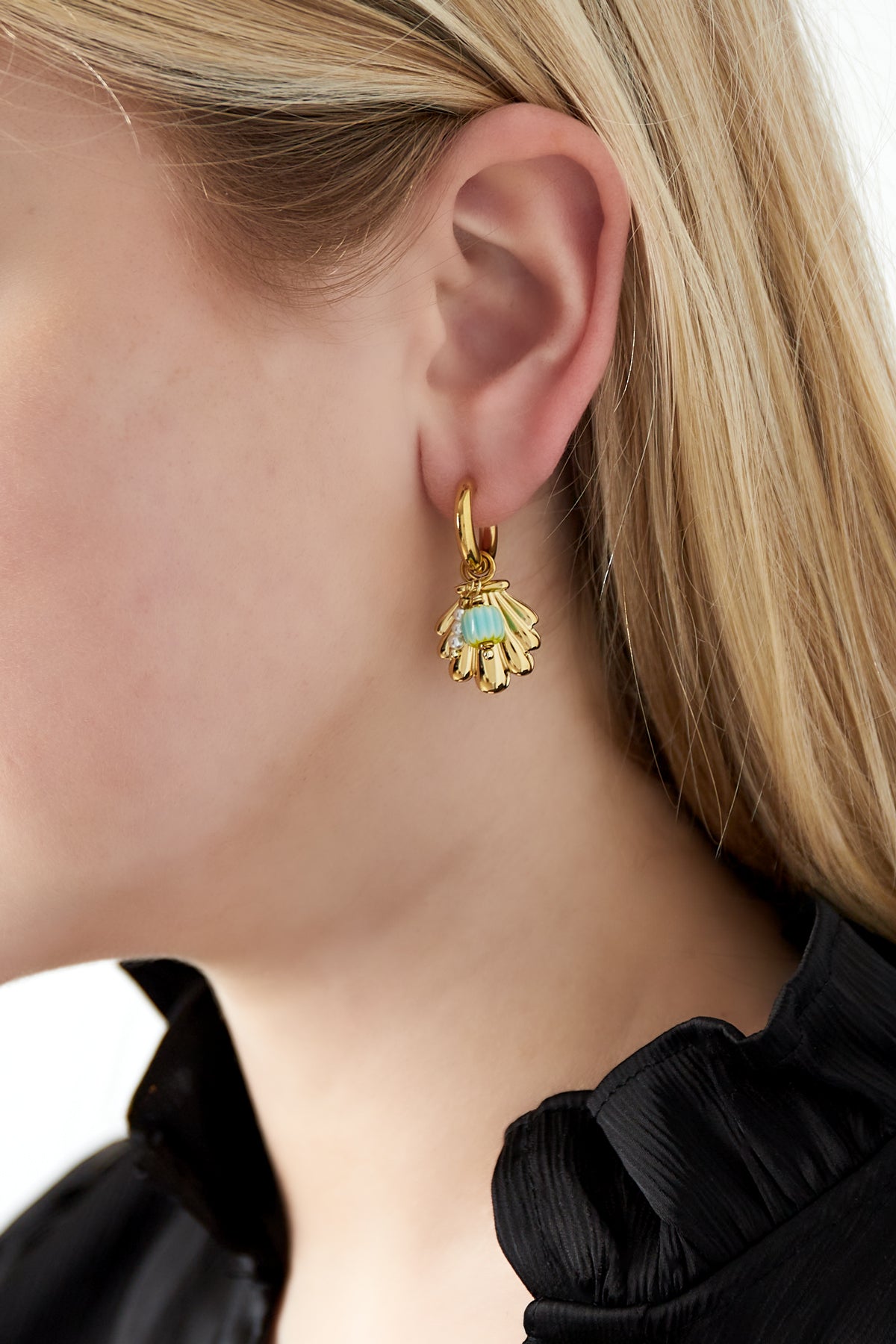 Close-up of a woman's ear wearing gold shell charm earrings with turquoise beads and pearls