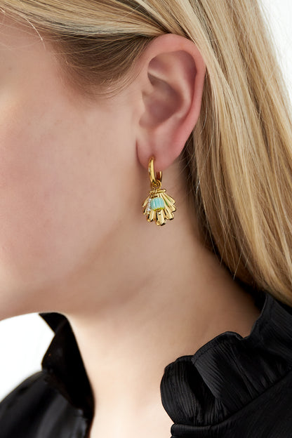 Close-up of a woman's ear wearing gold shell charm earrings with turquoise beads and pearls