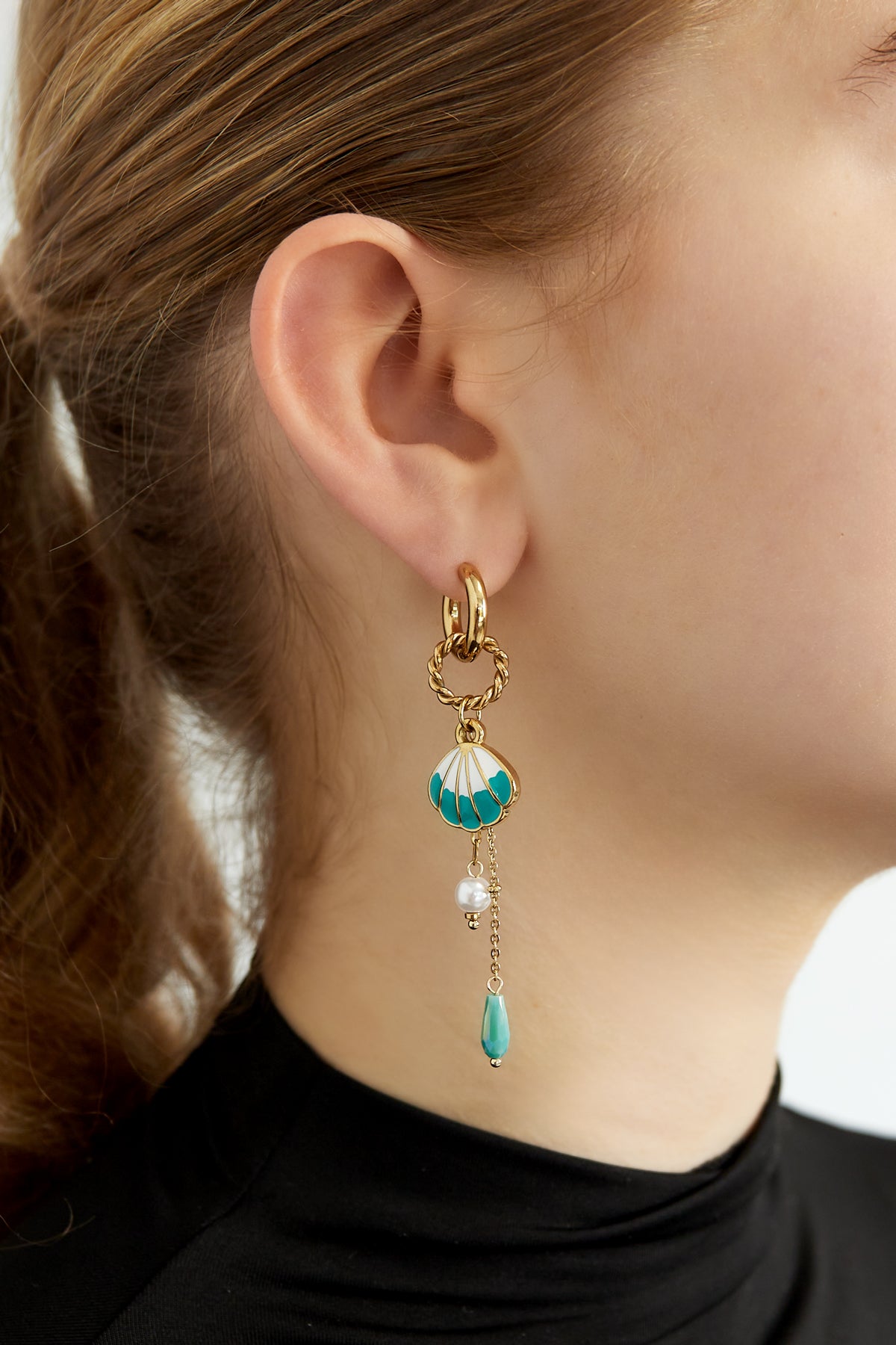 Close-up view of shell charm drop earring worn by a woman, showing detailed gold hoop, turquoise enamel shell, pearl and bead dangles