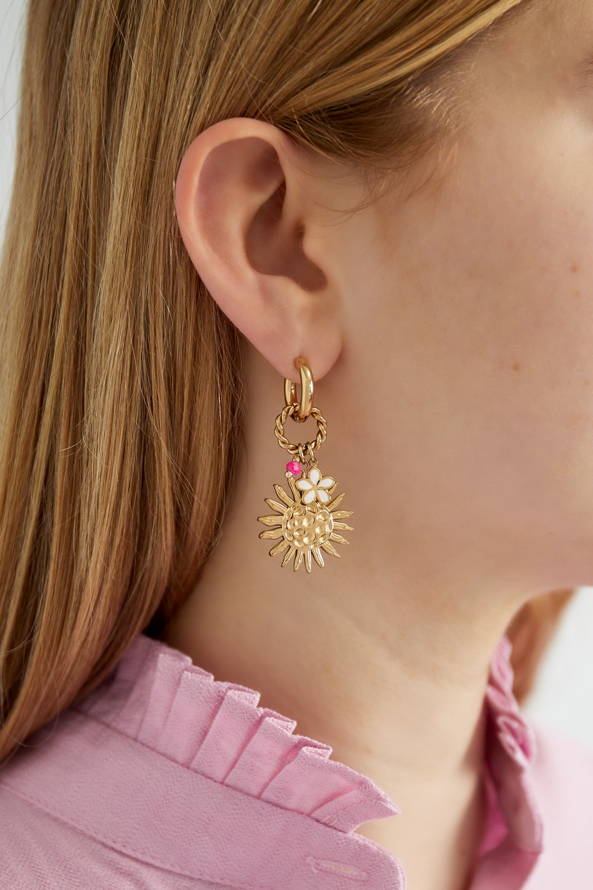 Close-up of model wearing gold-tone sunshine charm drop earring with white flower and pink bead detail, paired with a pink ruffled shirt.