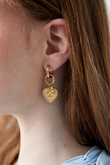 Gold heart charm hoop earring worn on ear with soft brown hair and light blue top