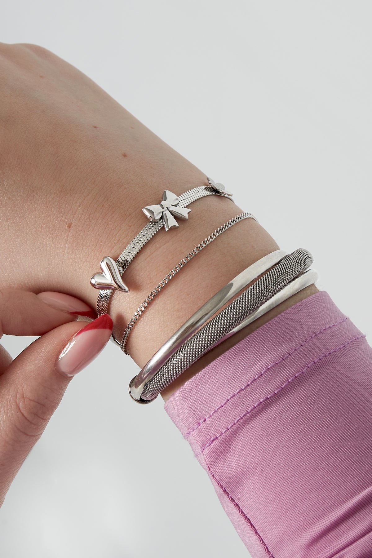 Close-up of wrist wearing silver charm bracelet with bow, heart, and flower charms alongside other metallic bracelets