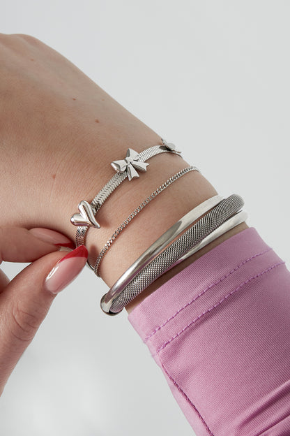 Close-up of wrist wearing silver charm bracelet with bow, heart, and flower charms alongside other metallic bracelets