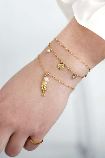 Woman's wrist wearing layered gold charm bracelets including heart, pearl and crystal charms