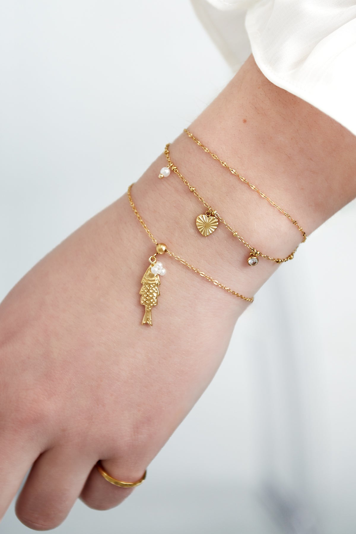Woman's wrist wearing layered gold charm bracelets including heart, pearl and crystal charms