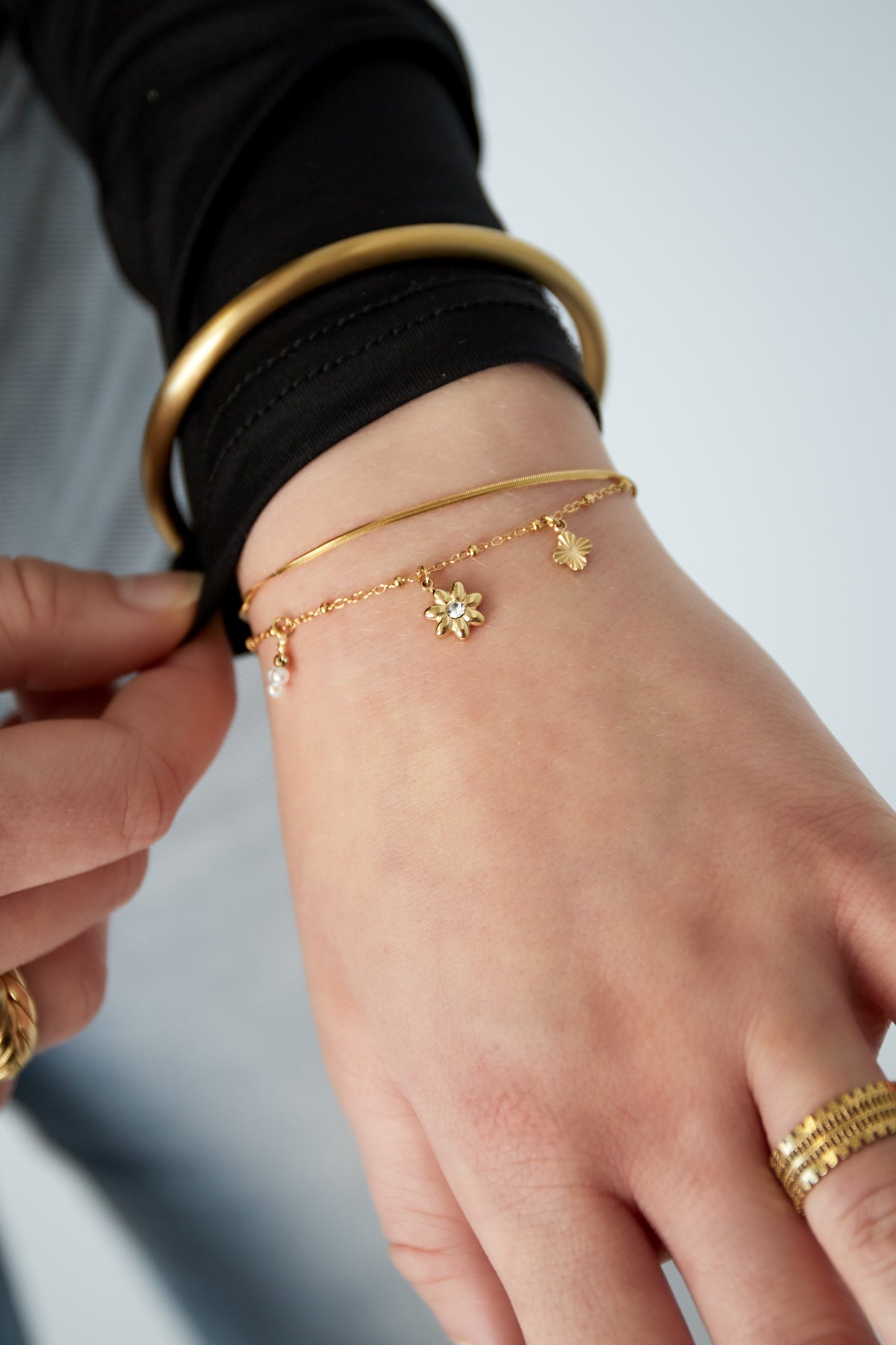 Woman wearing gold layered charm bracelet with floral and pearl charms and other gold bracelets