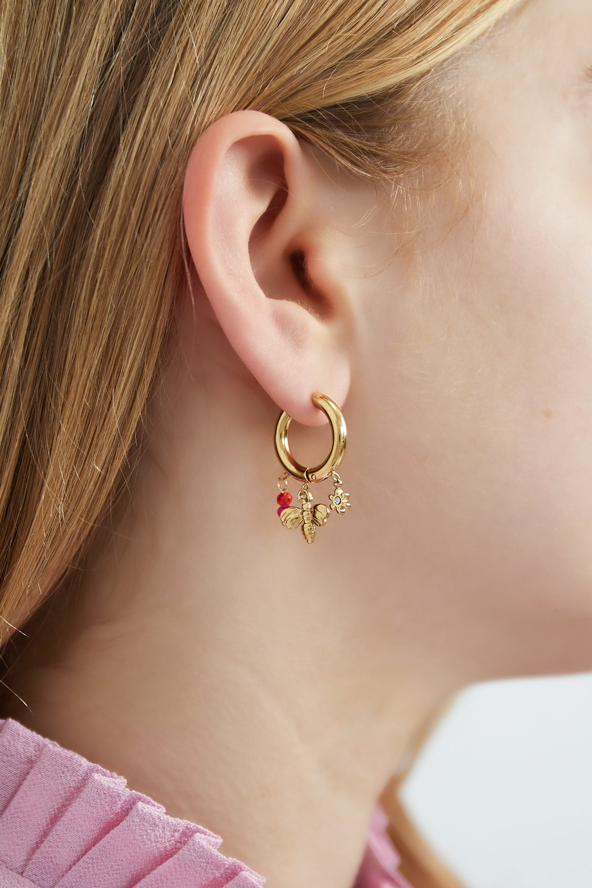 Model wearing gold charm hoop earring with bee, flower and red-pink beads