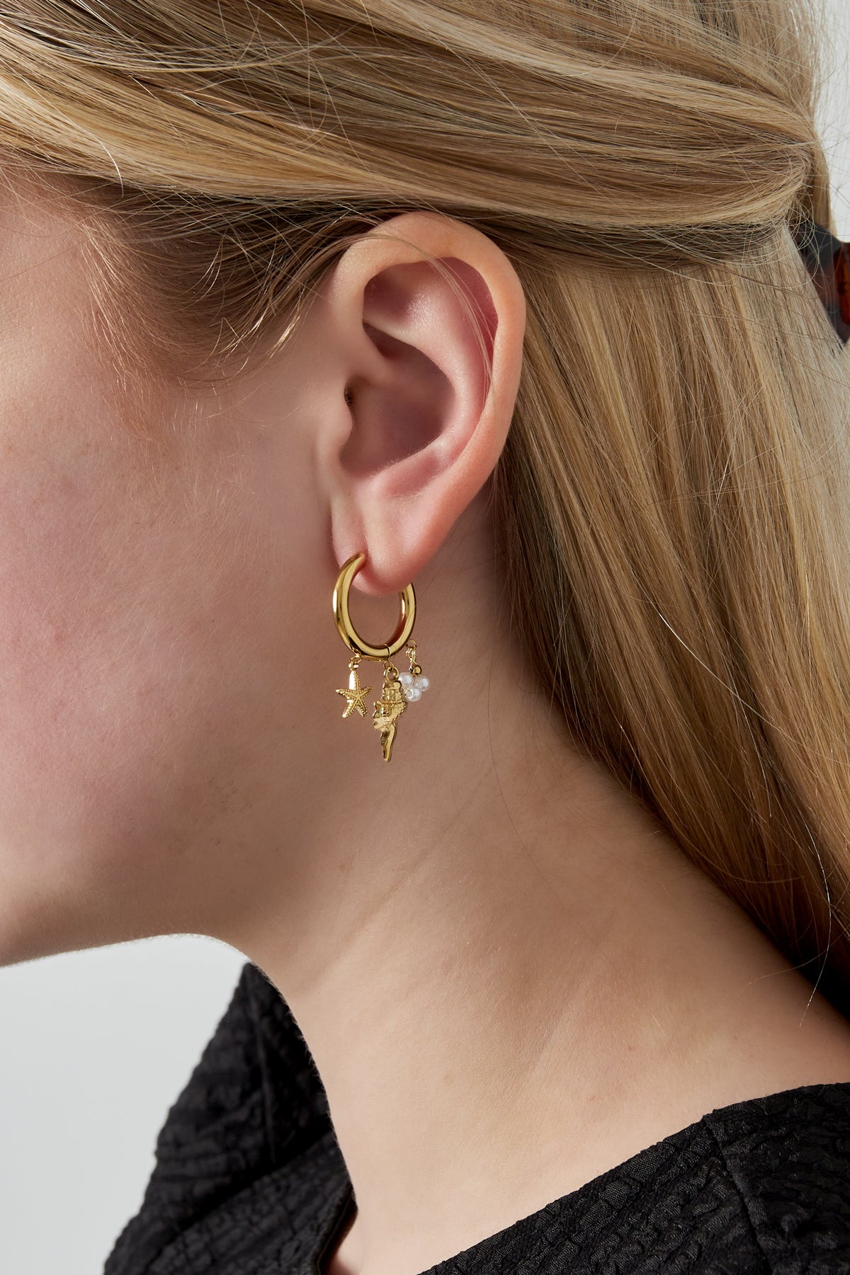 Model wearing gold hoop earrings with sea life charms, showing close-up on ear and blonde hair