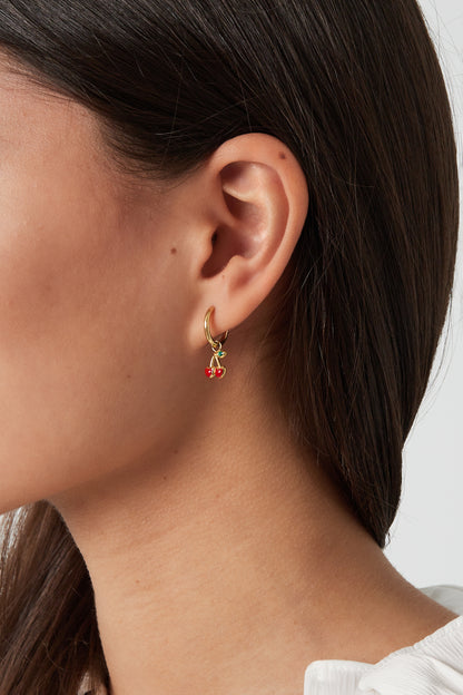Side profile of woman wearing gold hoop earrings with small red cherry charms