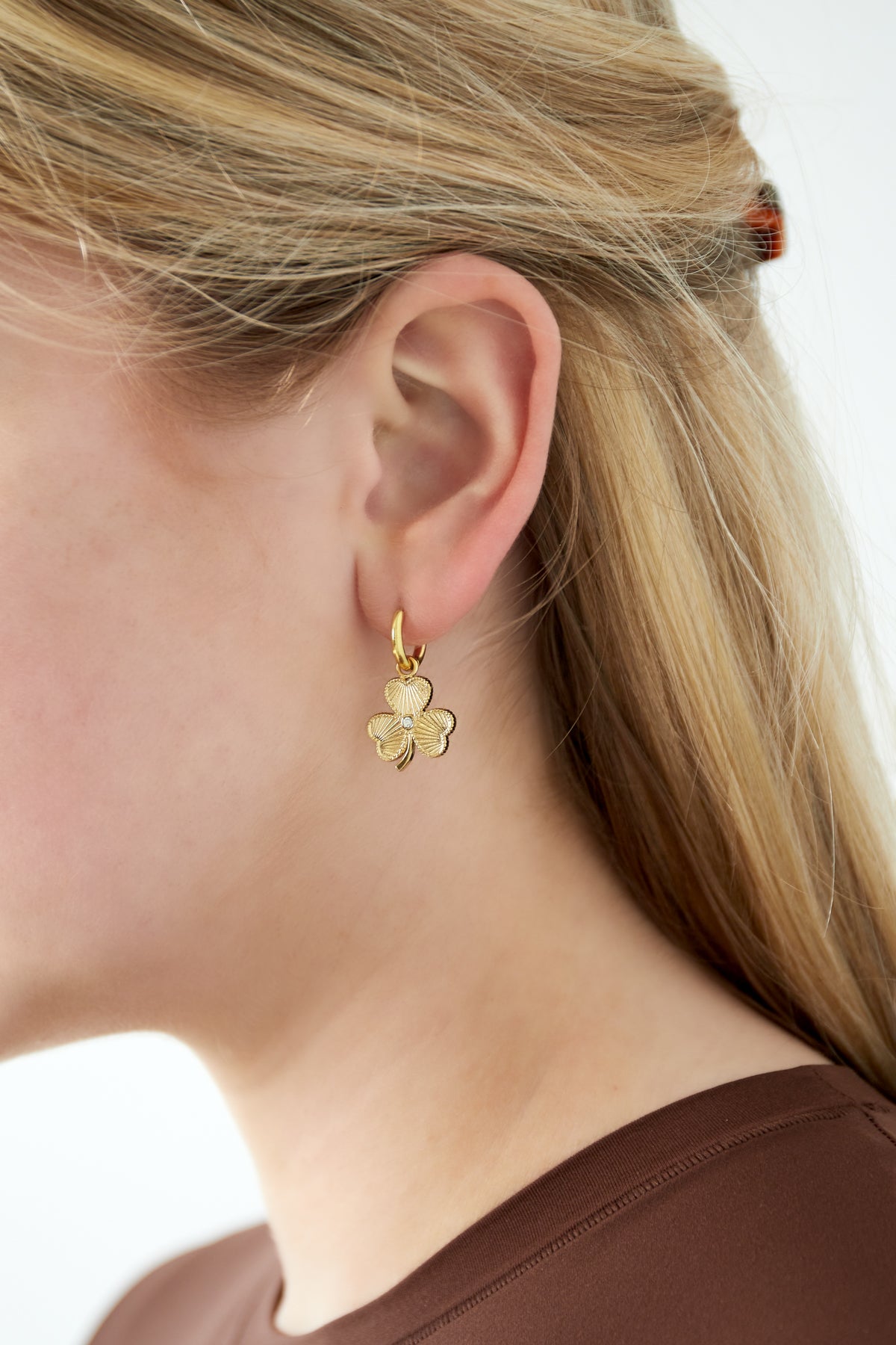 Close-up of woman wearing gold clover charm hoop earring showcasing charm detail