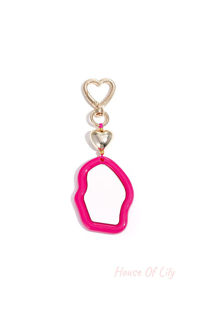 Vibrant pink acrylic irregular mirror charm with golden heart clasp on white background