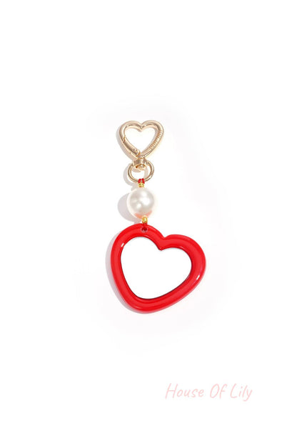 Close-up of gold heart-shaped clip holding red acrylic heart charm with pearl bead