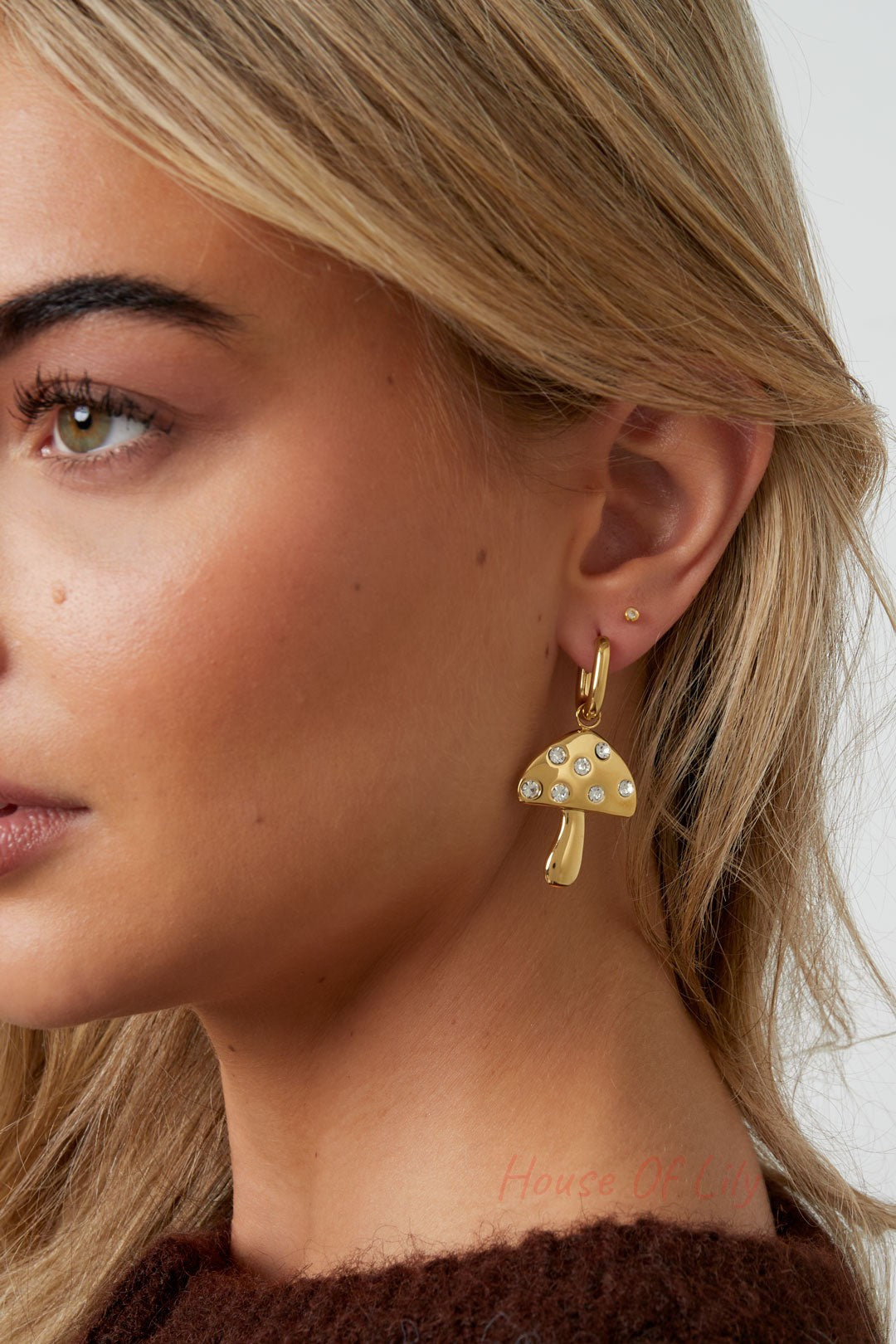 Close-up of a woman wearing one gold mushroom drop earring, showcasing the playful design