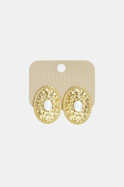Gold-tone oval stud earrings with hammered texture and pearl center attached to beige Lumé branded card