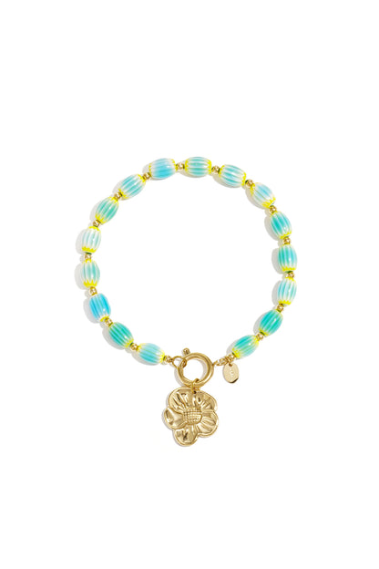 Turquoise and yellow striped beaded bracelet with gold-tone flower charm on white background