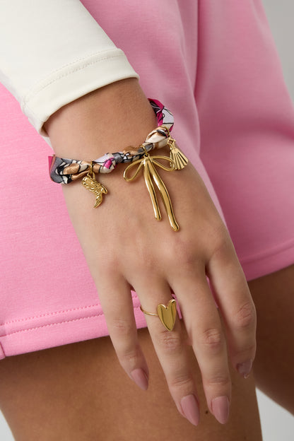 Bracelet worn on wrist paired with a gold heart-shaped ring and pink outfit, highlighting the playful and chic design