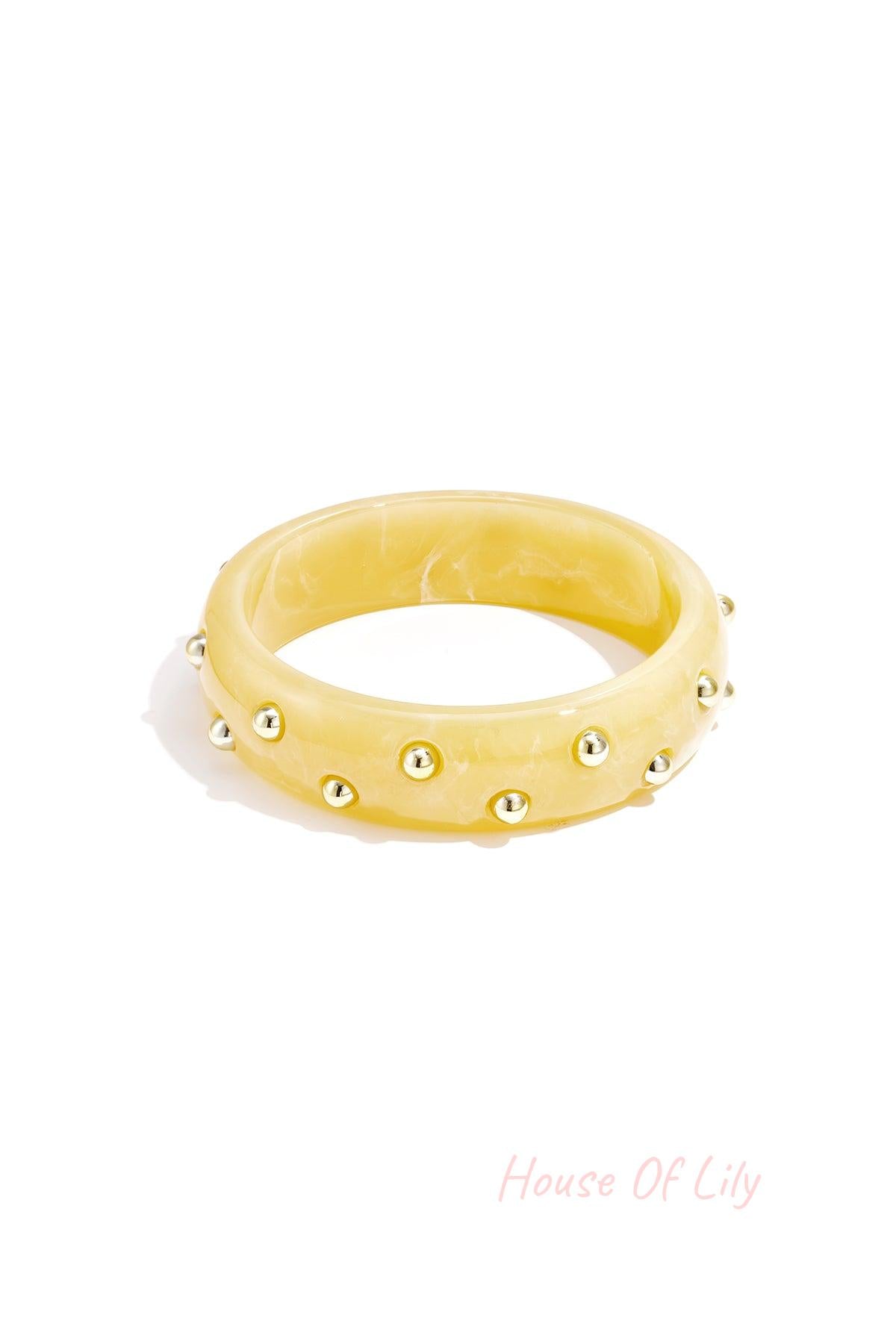 Yellow marbled resin bangle accented with gold studs on white background