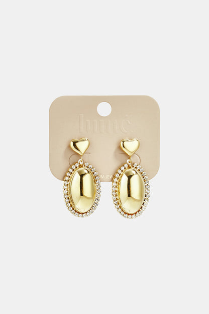 Gold oval drop earrings with crystal-encrusted borders and heart-shaped studs on a Lume jewelry display card.