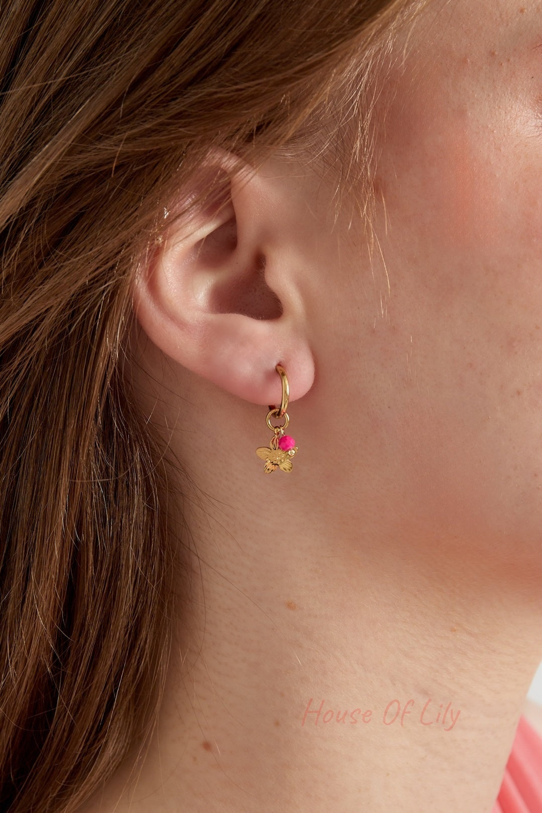 Gold floral charm hoop earring with bright pink bead worn on a woman's ear with brown hair