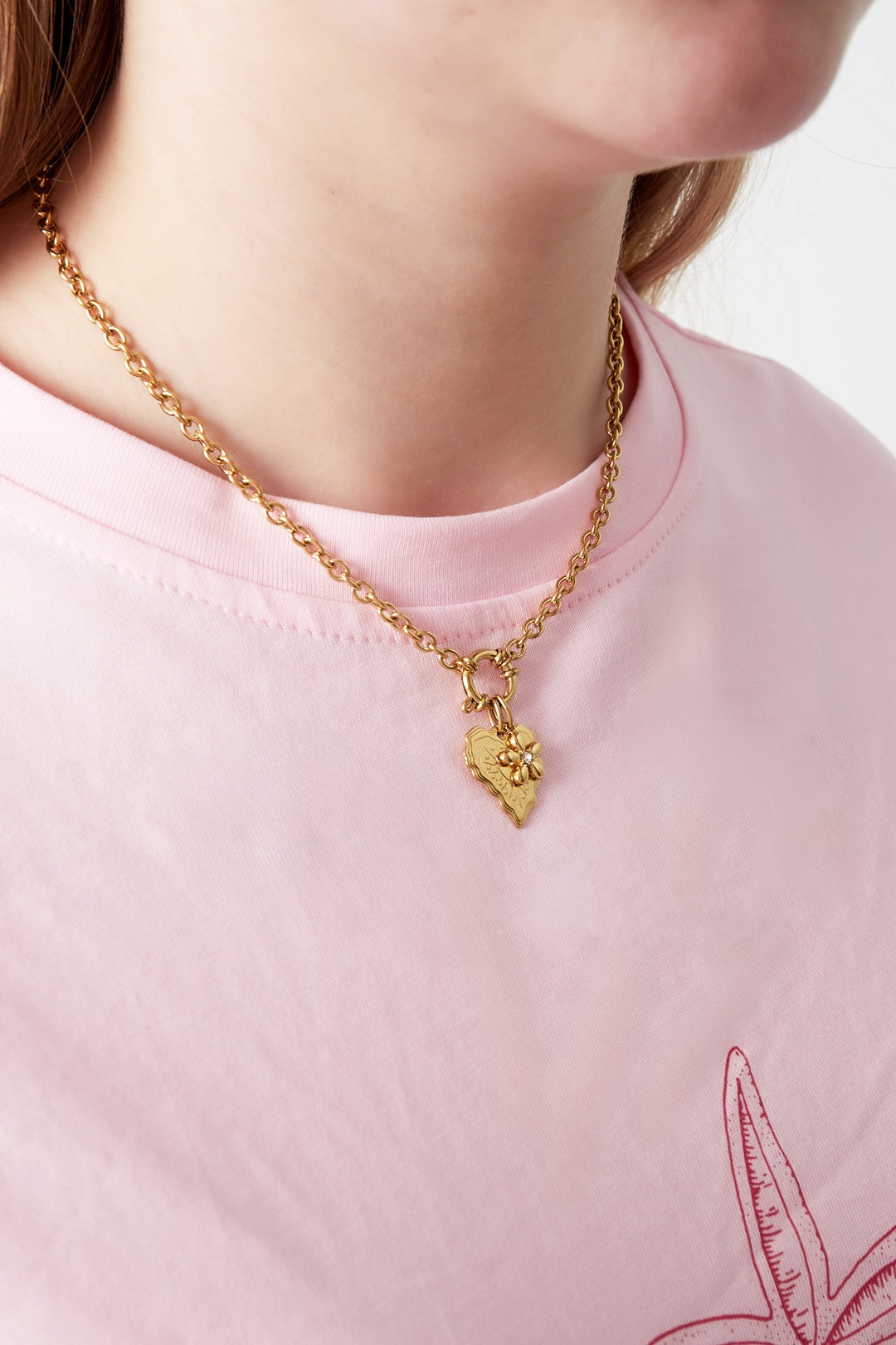 Close-up of a woman wearing gold charm pendant necklace over a light pink t-shirt with floral print