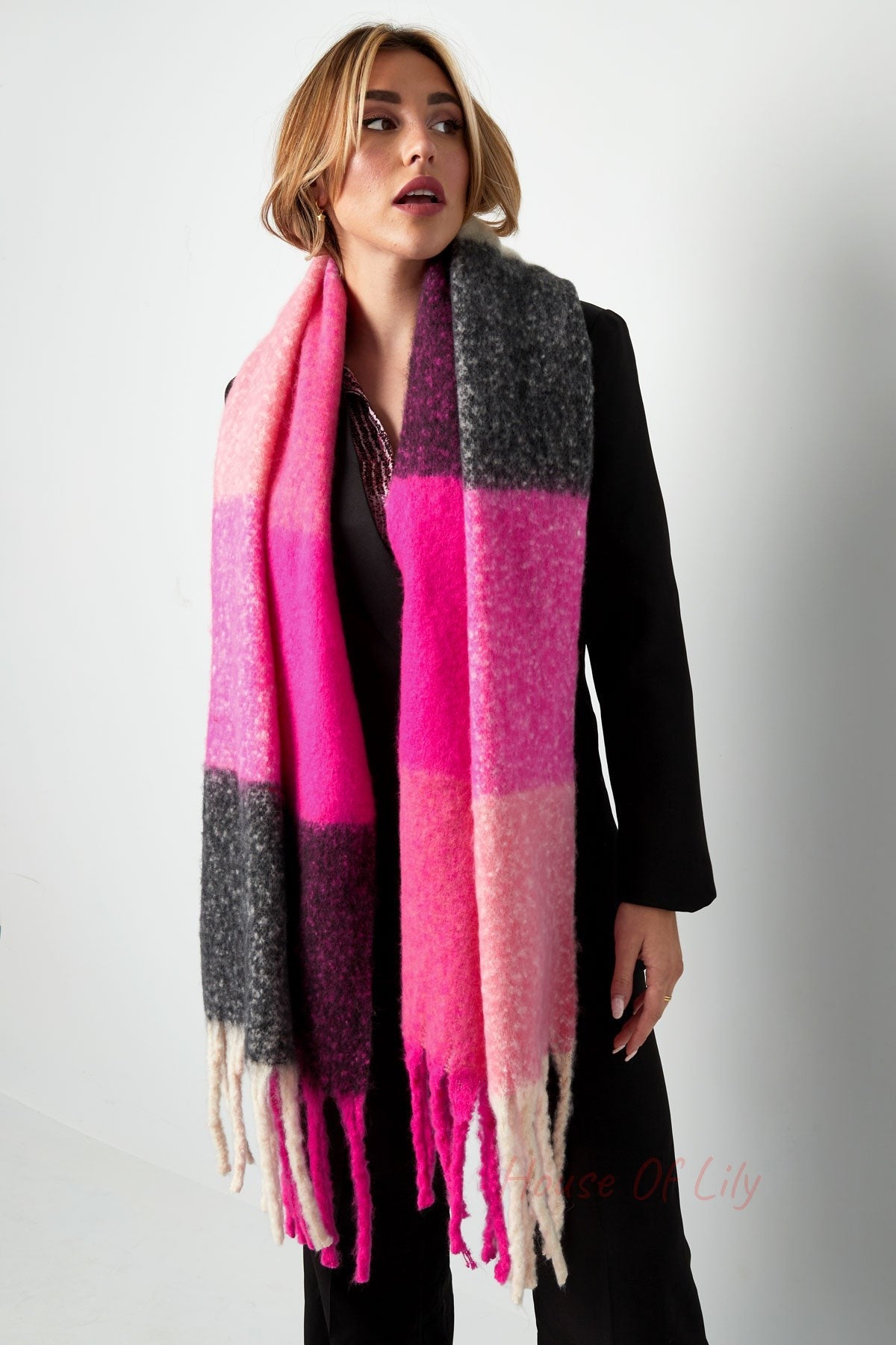 Woman facing forward wearing a bright pink and grey colorblock scarf with long fringes over black outfit
