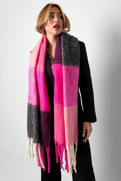 Woman facing forward wearing a bright pink and grey colorblock scarf with long fringes over black outfit