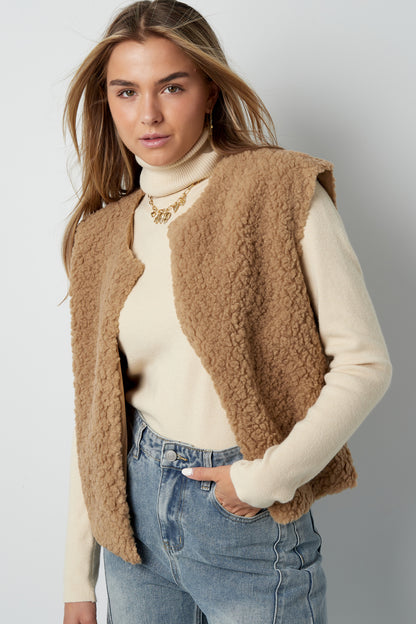 Model styled in camel sherpa vest layered over cream turtleneck sweater and light washed jeans
