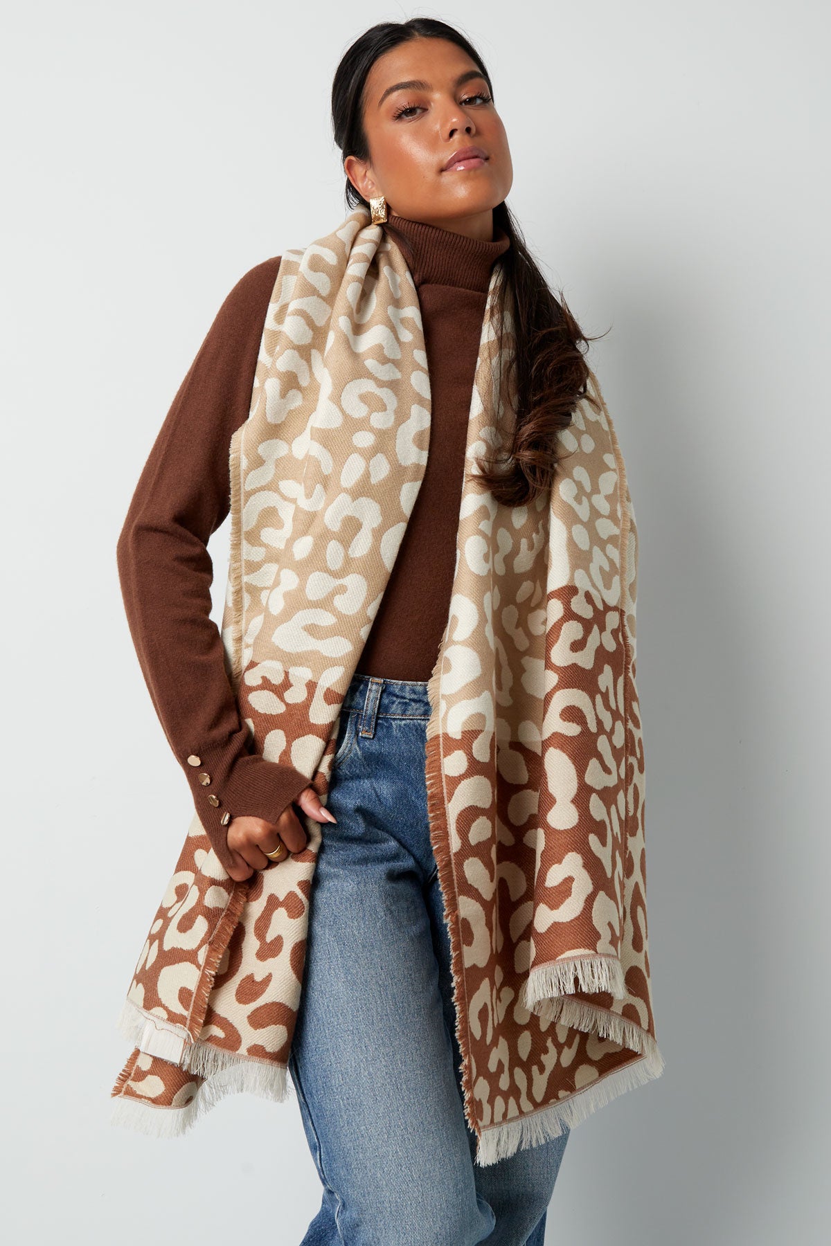 Model wearing an oversized beige and brown animal print scarf over a brown sweater and blue jeans