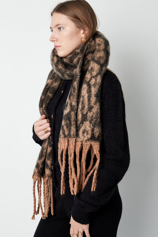Woman wearing a warm brown leopard print scarf with fringe, styled over black knitwear