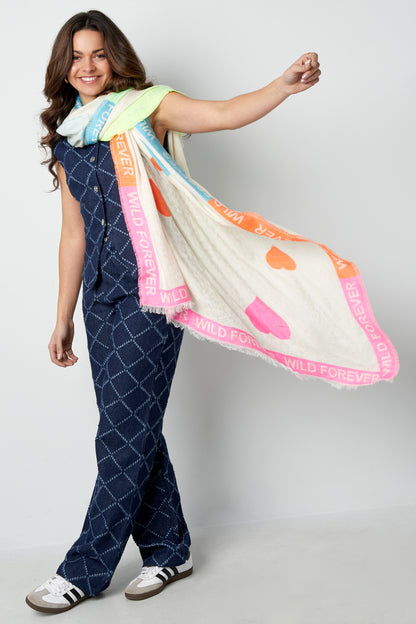 Woman wearing blue patterned jumpsuit modeling the colorful 'Wild Forever' scarf draped playfully around her shoulders