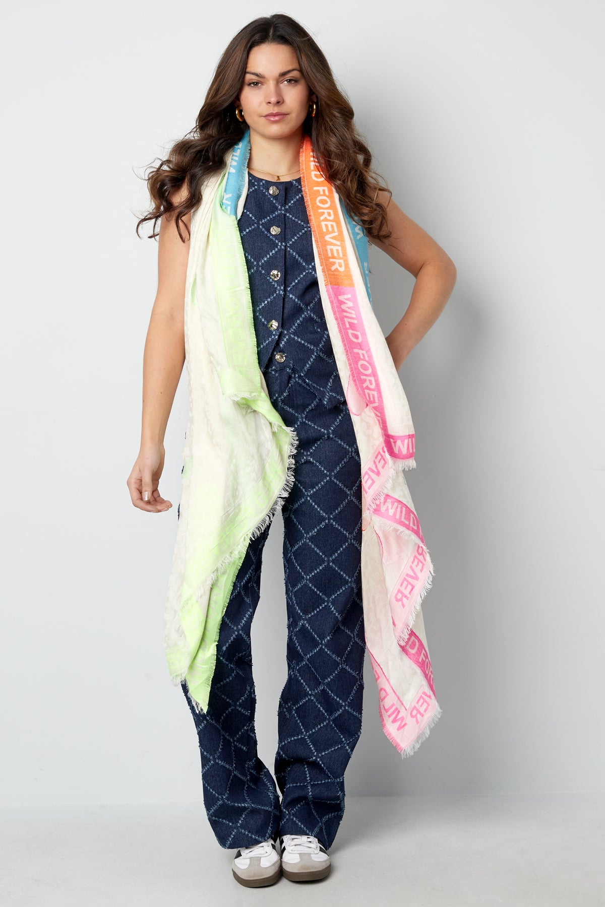 Front view of woman in blue patterned jumpsuit wearing the colorful 'Wild Forever' scarf casually draped around neck