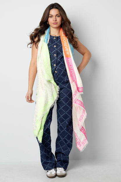 Front view of woman in blue patterned jumpsuit wearing the colorful 'Wild Forever' scarf casually draped around neck