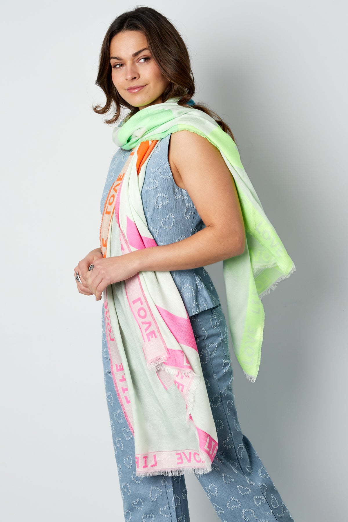 Female model smiling, posed side view wearing pastel scarf with LIFE LOVE text in pink, orange, and green colors