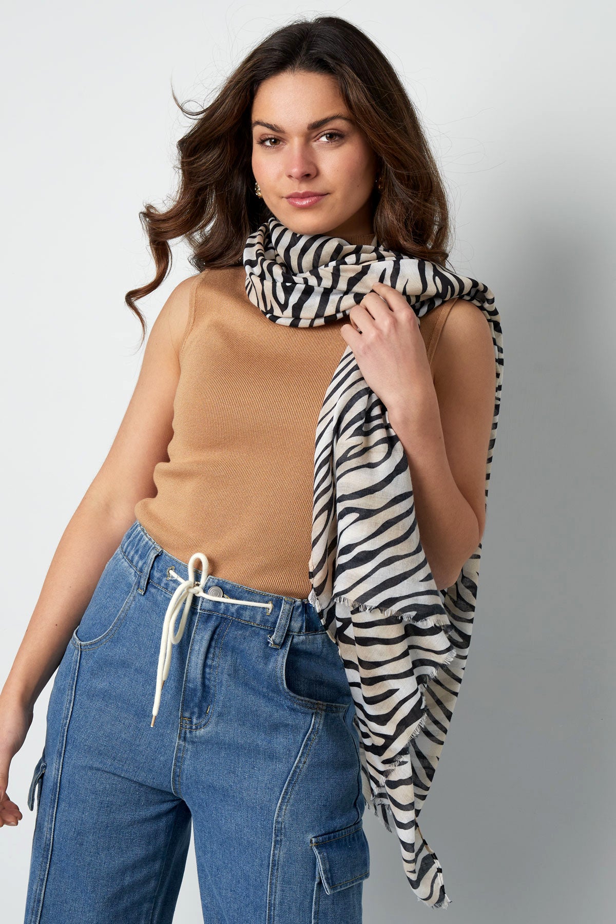 Woman wearing a zebra print scarf draped around her neck paired with tan sleeveless top and denim cargo pants