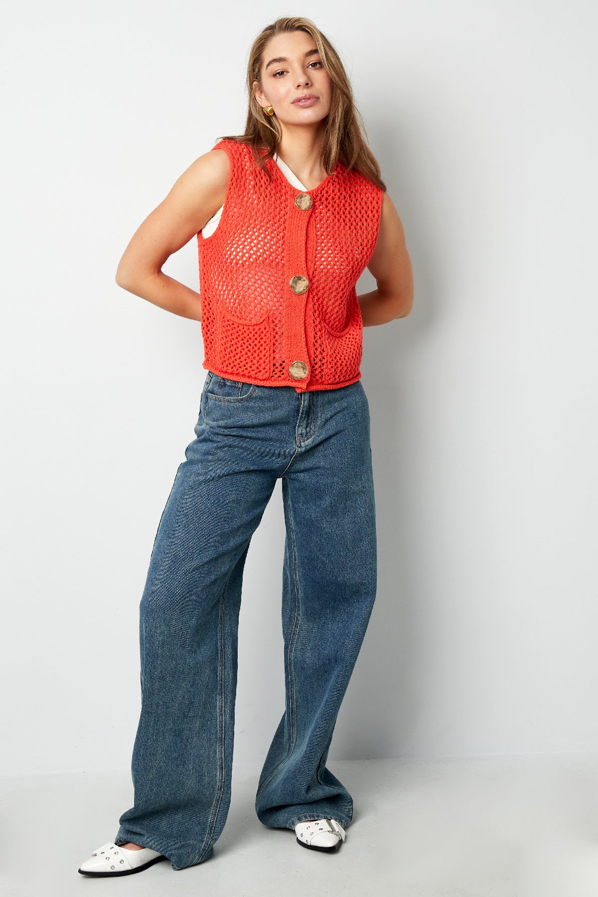 Model in bright red buttoned vest and jeans posing with hands behind back