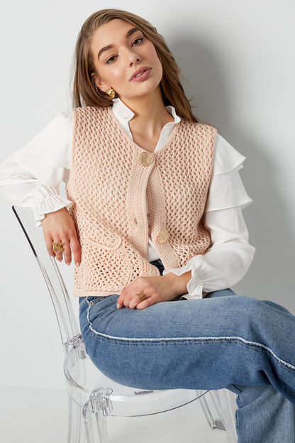 Back view of model showing beige knit vest with openwork pattern over leopard print top and jeans