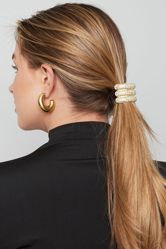 Side view of woman with blonde hair wearing the crystal gold-tone hair elastic securing a low ponytail, paired with chunky gold earrings