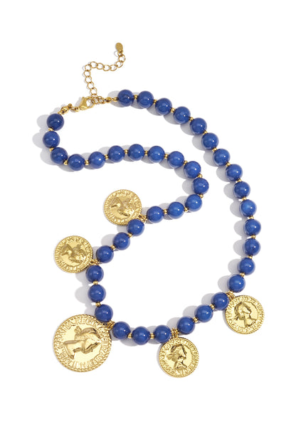 Flat lay of navy blue acrylic beaded necklace with gold-tone vintage coin pendants on white background