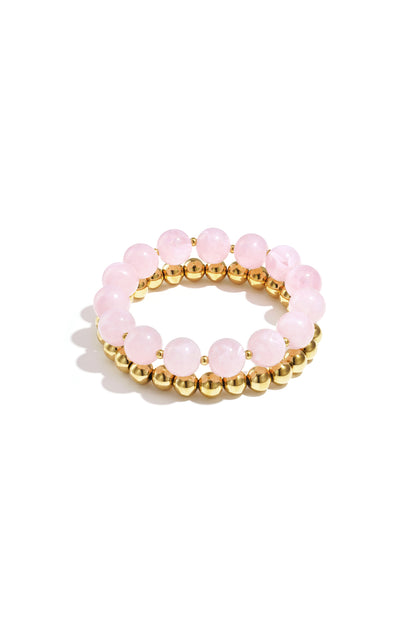 Stack of two bracelets with soft pink round acrylic beads and gold-tone metal beads on white background