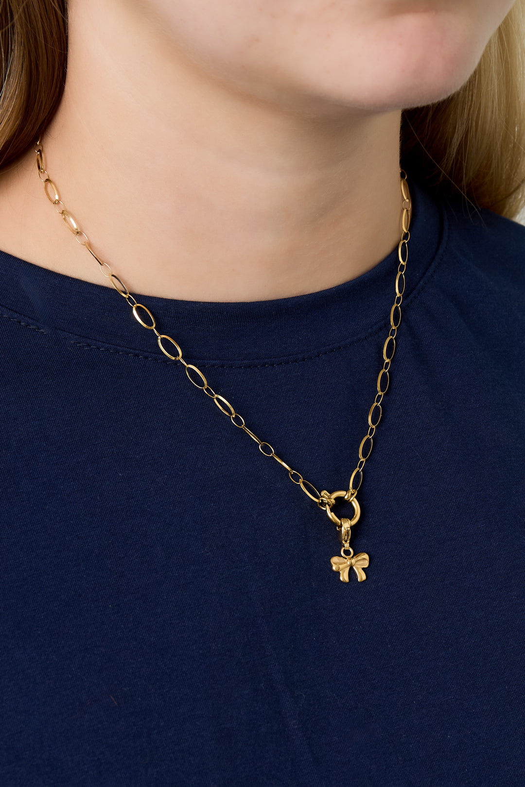 Model wearing gold link necklace with small gold bow charm pendant over a navy blue top