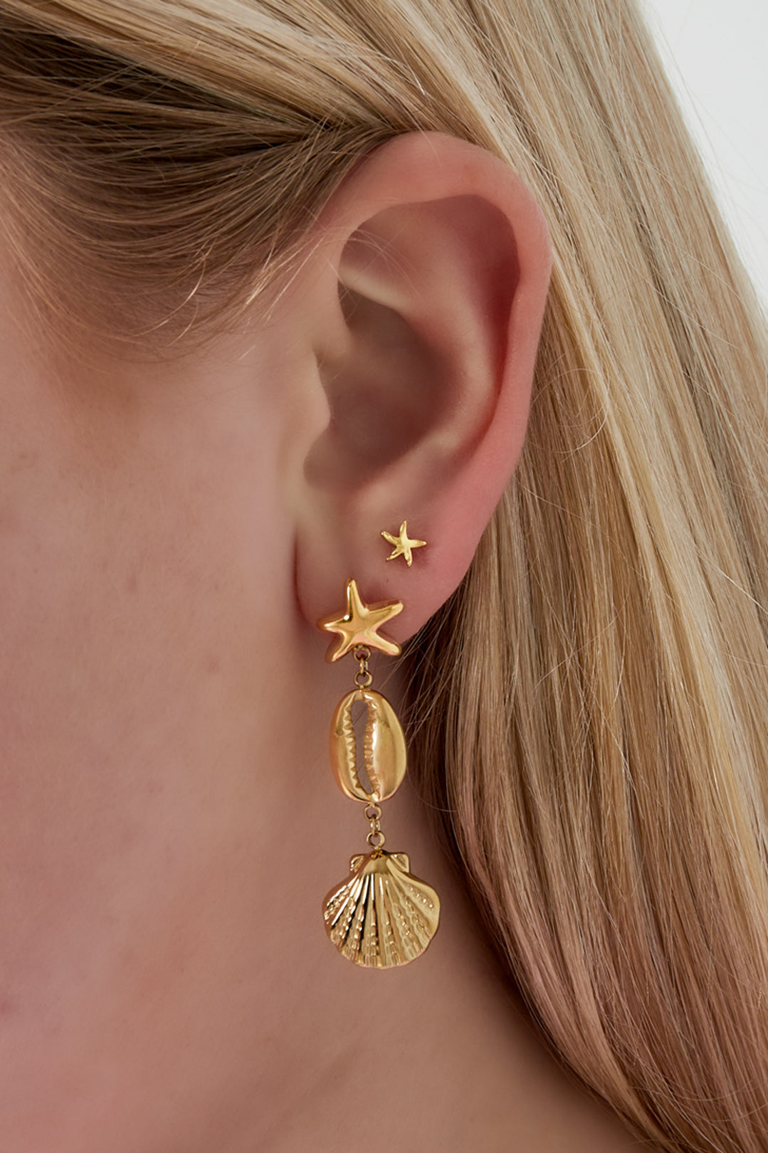 Close-up of a woman wearing gold-tone starfish stud earring and layered ocean-themed dangling earrings